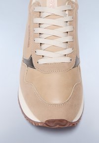 Sneaker beige con materiali in pelle texturizzata e suede, punta rotonda, lacci beige e suola in gomma marrone con motivo a onde.