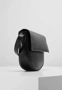 Borsa in pelle nera di forma arrotondata, con chiusura a pattina e manico laterale. Texture liscia con cuciture bianche a contrasto lungo i bordi.