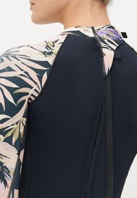 Svart våtdrakt med blomsterdekorert ermer. Har glidelås og stroppdetaljer på baksiden, laget av dekkende, elastisk materiale.