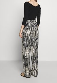 Černý žebrovaný top s dlouhým rukávem, který je spárován s vysokým pasem a širokými nohavicemi s vertikálním proužkovaným vzorem v černobílé barvě.