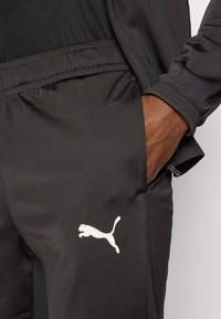 Μαύρο αθλητικό παντελόνι από απαλό ύφασμα, με ελαστική μέση και λευκό λογότυπο Puma στην αριστερή πλευρά.