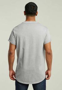 Jasnoszara koszulka z krótkim rękawem z podwiniętymi rękawami, z miękkiego materiału i zaokrąglonym dołem, noszona z ciemnymi dżinsami, widok z tyłu.