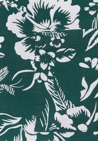 Tumma vihreä kangas, jossa on suuria valkoisia kukka- ja lehtikuvioita yksityiskohtaisilla ääriviivoilla, luoden elävän, kontrastisen suunnittelun.