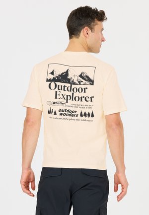 Mann mit dem Rücken zur Kamera, trägt ein beiges T-Shirt mit Berggrafik und Text "Outdoor Explorer" sowie schwarze Hose vor einfarbigem Hintergrund.