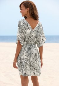 Kurzärmeliges, knielanges Kleid in Weiß mit schwarzem Blättermuster. Verfügt über einen V-Ausschnitt und eine Bindegürtel-Detail an der Taille. Glatter Stoff mit fließender Silhouette.