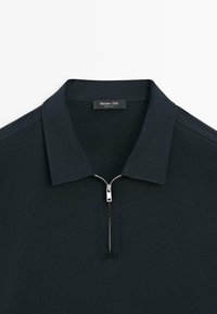 Czarna koszula z kołnierzykiem, wyposażona w srebrny zamek na pół oraz metkę marki "Massimo Dutti" wewnątrz kołnierza.