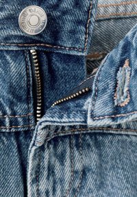 Denim odjeća s metalnim srebrnim kopčom, otkrivenim patentnim zatvaračem, plavom tkaninom s izblijedjelim dijelovima i kontrastnim narančastim šavovima.
