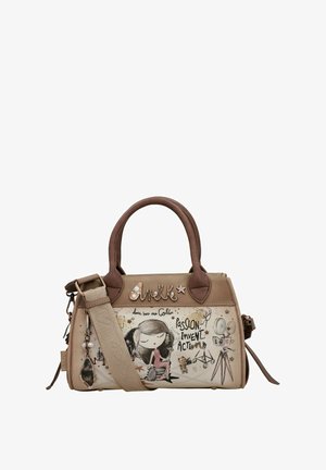 Beige Handtasche mit braunen Akzenten, featuring ein grafisches Design eines Mädchens im Rollstuhl, Textmuster und einem abnehmbaren Riemen.