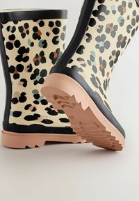 Bottes de pluie en caoutchouc à imprimé léopard avec une base crème, des accents noirs et une semelle texturée rose avec un motif en zigzag.