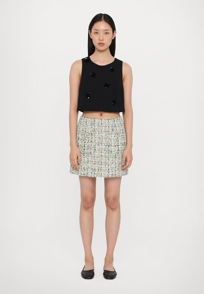 Black sleeveless crop top with floral embellishments, paired with a woven mini skirt featuring multicolored threads. Fitted design, flat shoes.