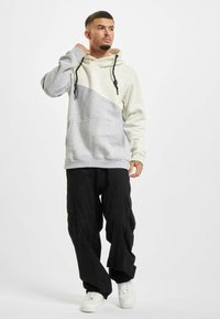 Gray and cream color-blocked hoodie with a front pocket, textured fabric, adjustable black drawstrings, and paired with black cargo pants.