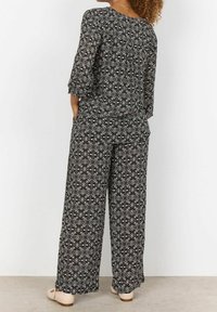 Sort og hvidmønstret jumpsuit med trekvartærmer, løst fit og brede bukser. Har en blød, tekstureret stof.