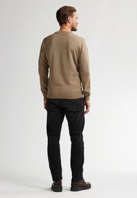 Maglione a maglia marrone con scollatura a girocollo, maniche lunghe e polsini a costine, abbinato a jeans in denim neri e scarpe stringate marroni.