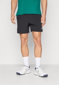 Pantalones cortos deportivos negros con cintura elástica, textura suave y un pequeño logo. Se llevan con calcetines blancos y zapatillas blancas con acentos en azul marino.