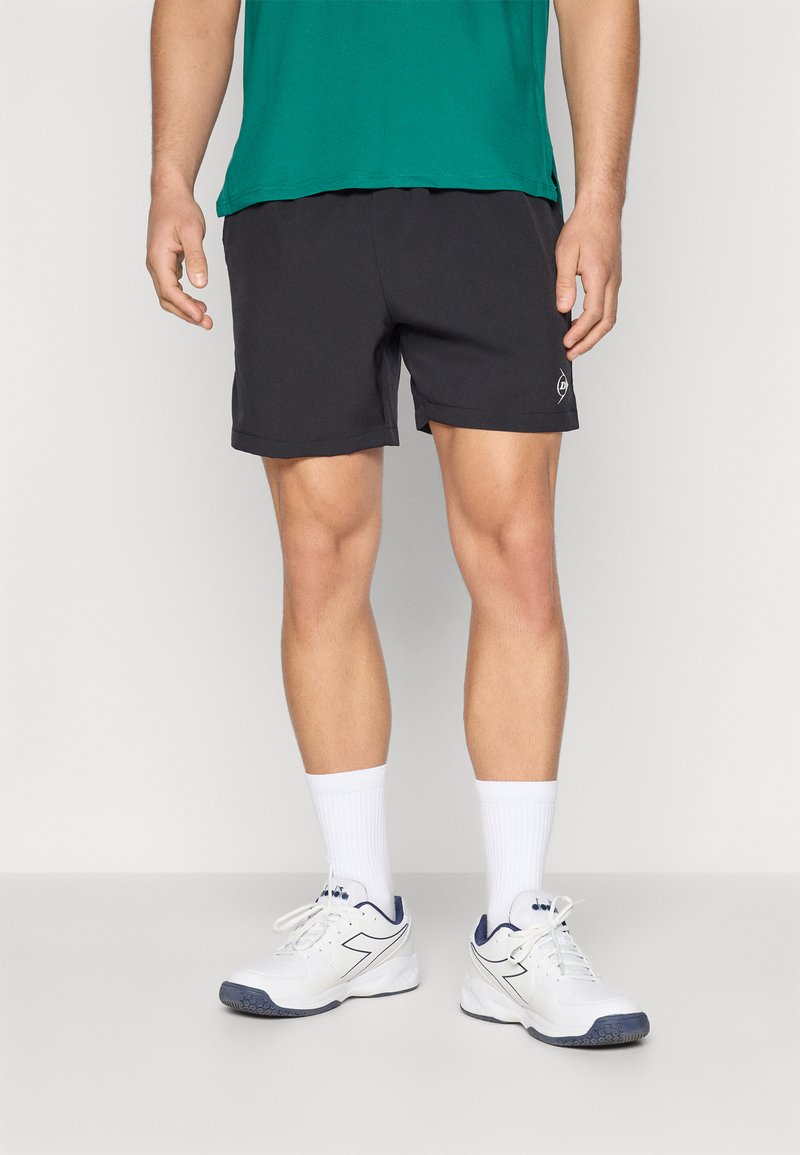 Pantalones cortos deportivos negros con cintura elástica, textura suave y un pequeño logo. Se llevan con calcetines blancos y zapatillas blancas con acentos en azul marino.