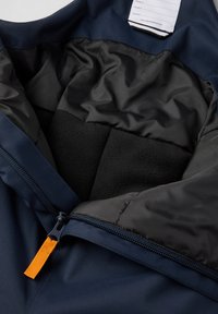 Marineblauwe jas met zwart geïsoleerd voering, oranje ritslus, en wit label met tekst in het gedeelte van de kraag.