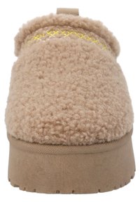 Zapatilla beige con material superior esponjoso y texturizado, con un detalle de costura amarilla y una suela gruesa de goma. Diseño redondeado.