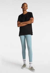 T-shirt in cotone nero con logo in rilievo, abbinato a leggings azzurri aderenti con cuciture a contrasto, indossato con scarpe slip-on a scacchi bianche e nere.