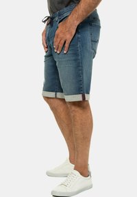 Shorts de mezclilla en un lavado azul medio. Con cinturilla ajustable, dobladillo enrollado y costuras en contraste. Combinados con zapatillas blancas.