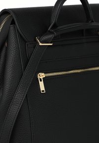 Musta nahkainen reppu, jossa on teksturoitu viimeistely, kullanvärinen vetoketju ja metalliosat, etutasku vetoketjulla ja kahdet kahvat.