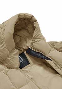 Giacca isolante beige con colletto alto, tessuto texture e cerniera. Etichetta interna con il nome del brand visibile nella zona del collo.