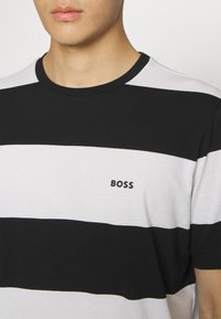 Juodai balta dryžuota marškinėliai su apvaliu iškirpimu ir mažu "BOSS" logotipu ant krūtinės, pagaminti iš lygios medvilnės mišinio audinio.
