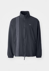 Giacca a zip grigia scura realizzata in tessuto testurizzato, con tre strisce verticali e tasche laterali. Polsini e fondo elastici.