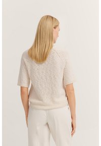 Cremfarbener kurzärmeliger Strickpullover mit strukturiertem Muster, gerippten Bündchen und Saum. Die Rückansicht zeigt eine lässige Passform und nahtlose Schultern.
