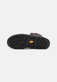 Semelle de botte de randonnée marron avec un profil agressif en caoutchouc noir, présentant des rainures et un accent jaune distinct au centre pour une meilleure traction.