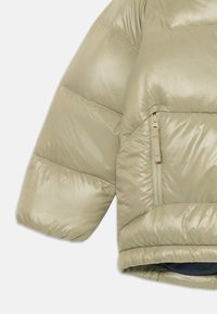 Giacca puffer verde oliva chiaro con finitura lucida, dotata di una tasca con zip e maniche corte e larghe, che mostrano un'imbottitura trapuntata.