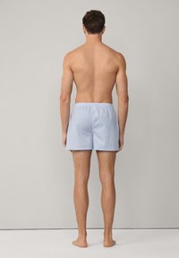 Ljusblå bomullssimshorts med elastiskt midjeband, med ett subtilt mönster. Synligt från baksidan.