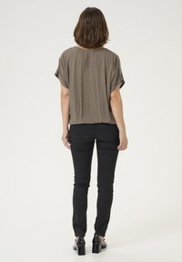 Top marrone, largo e con maniche corte, con scollatura rotonda, abbinato a jeans neri a taglio slim e scarpe con tacco nere.