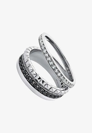 Tres anillos apilados: uno de plata con piedras transparentes, uno con piedras negras y acentos en forma de pirámide, y uno de banda texturizada en plata.