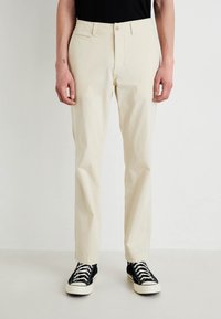Pantaloni din bumbac bej cu un design drept, având buzunare laterale și închidere cu nasture, asortați cu adidași negri cu guler înalt.