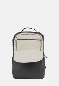 Svart läderryggsäck med en texturerad yta, som har ett dragkedjad fack och en ljusbeige interiör. Designen är funktionell med en framficka.
