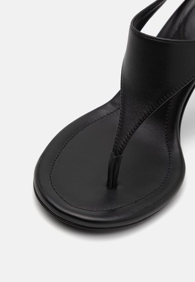 Sandal cu brâu din piele neagră, cu o suprafață netedă, talpă plată și design minimalist, având o curea îngustă între degete.