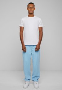 White cotton t-shirt paired with light blue corduroy pants. Model wears white sneakers; standing against a neutral gray background.