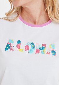 White cotton t-shirt with a light pink neckline. The text "ALOHA" is printed in colorful floral patterns featuring blue, pink, and yellow flowers.