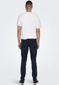 Vit t-shirt med kort ärm kombinerad med mörkblå denimjeans, som ger en slim fit och har bakfickor. Svartvitrandiga sneakers fulländar looken.