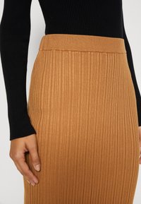 Jupe en tricot à côtes de couleur beige chaud, dotée d'une taille ajustée et d'un design long et droit. La texture est lisse avec des rayures verticales.