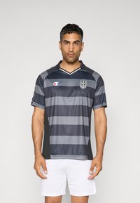 Grijze en zwarte gestreepte voetbalshirt met een kraag, korte mouwen en een logo op de borst; gecombineerd met witte shorts.