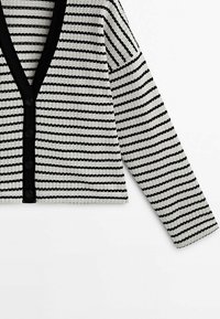 Cardigan rayé noir et blanc avec un col en V, fermeture par boutons et manches longues. Le tissu a une texture côtelée et une bordure noire contrastante.