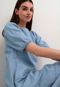 Gaišzila džinsa kleita ar īsām puff piedurknēm, mīksta tekstūra un brīvs griezums, ar apaļu dekoltē un minimālām uzšuvēm.