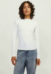 Valge pika varrukaga ribatekstiilist topp ümmarguse kaelusega, veidi lühendatud äärega ja struktuurse viimistlusega, koos siniste teksadega.