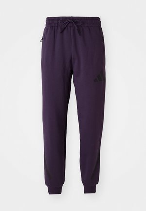 Lilla joggebukser laget av myk bomullsblanding. Har elastisk midje med snor og glidelåslommer på siden. Svart detaljer på beina.