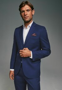 Marineblauer Anzug aus strukturiertem Stoff, einreihige Jacke, Reverskragen und kontrastierendes weißes Hemd. Enthält ein burgunderfarbenes Einstecktuch.