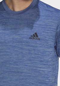 Sininen urheilu paita, jossa on rakenteellinen, harjattu kuosi. Varustettu pyöreällä kaula-aukolla ja mustalla Adidas-logolla rinnassa.