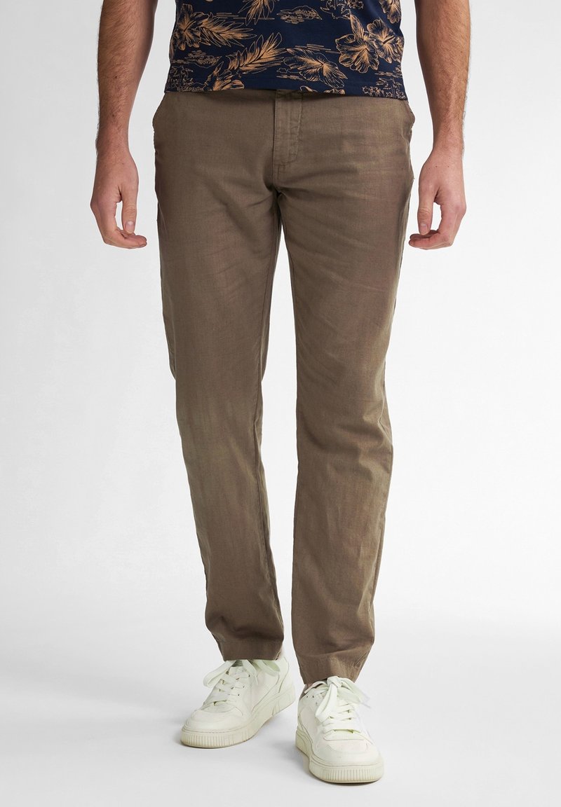 Pantaloni di lino marrone chiaro con una texture liscia, vestibilità affusolata e tasche laterali, abbinati a sneaker bianche e una camicia floreale blu navy.