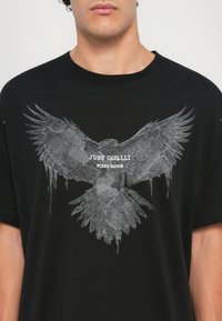 Svart bomulls t-skjorte med et stort grått hauk grafikk og teksten "JUST CAVALLI" og "FIRED EARTH" under fuglen. Korte ermer.