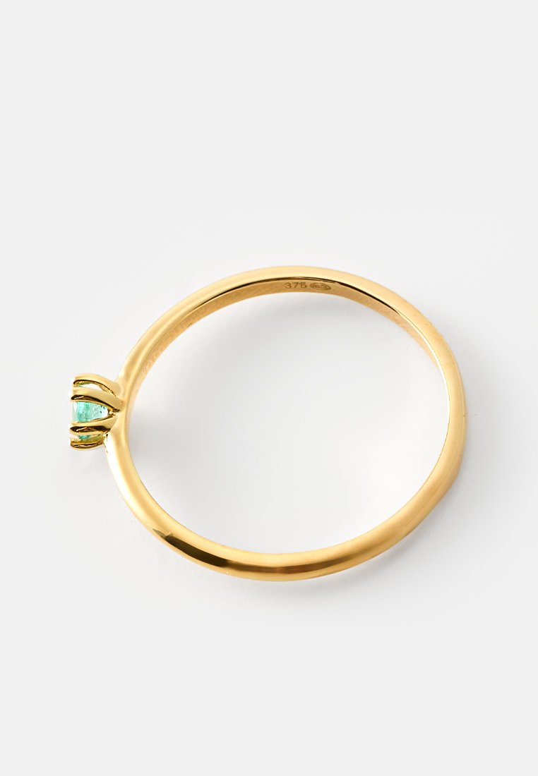 Goldring mit einem kleinen grünen Edelstein, gehalten von vier Krappen, vor einem weißen Hintergrund gezeigt.